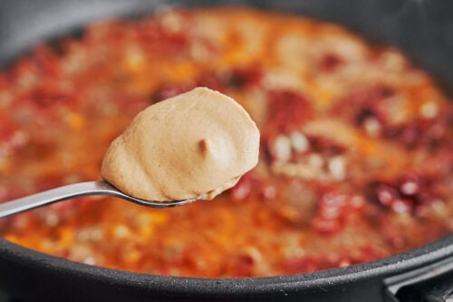 a spoon of Dijon mustard being added to the skillet sauce