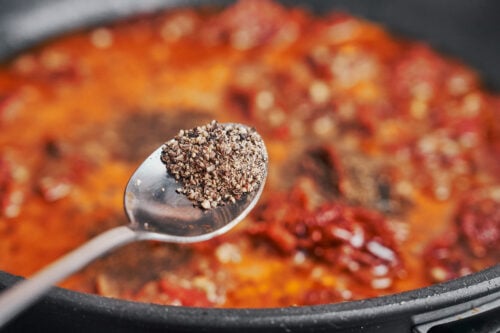 seasoning the sauce with freshly ground black pepper