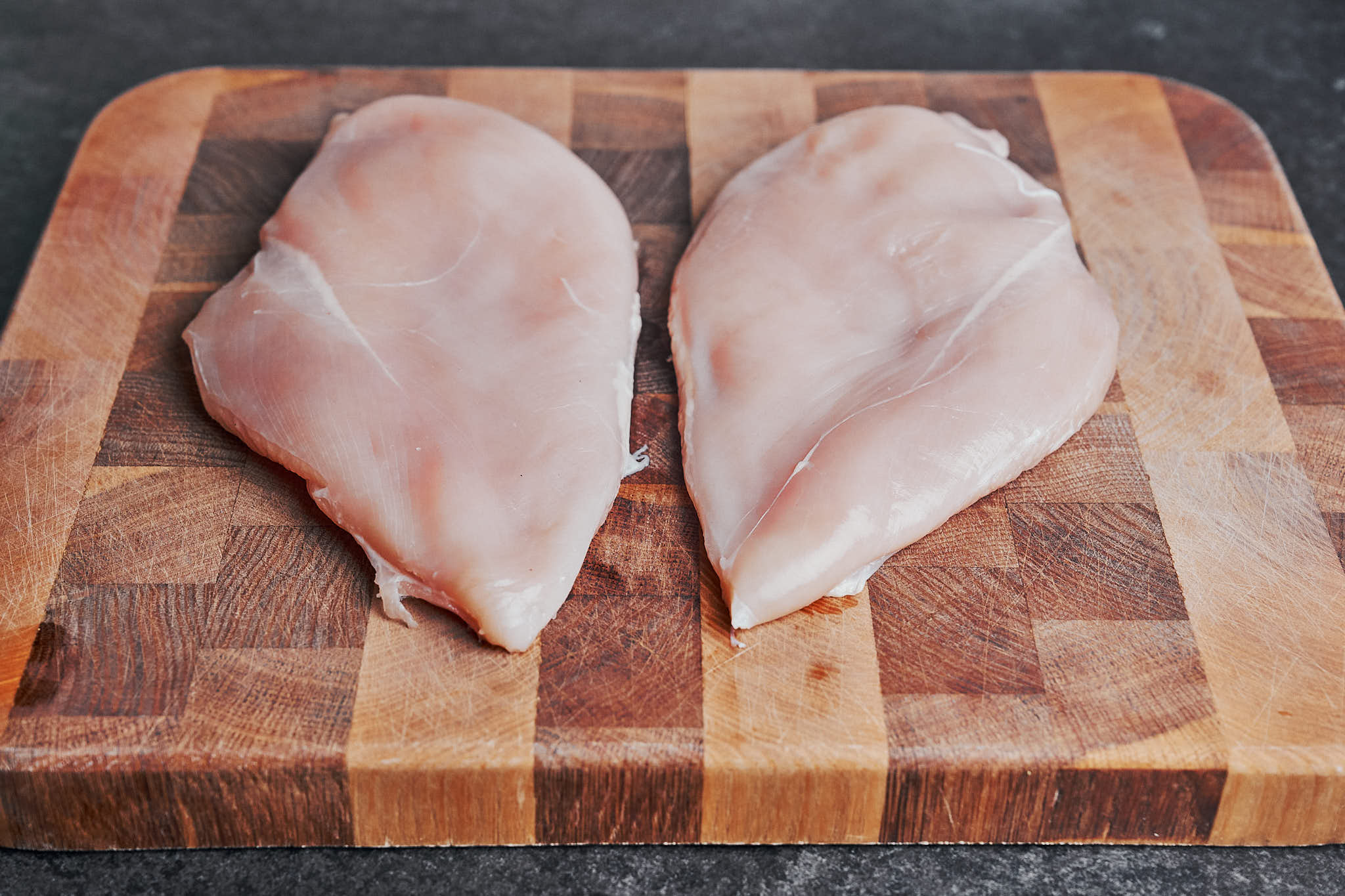 raw chicken breasts on a wooden cutting board ready to be sliced for creamy sun dried tomato chicken
