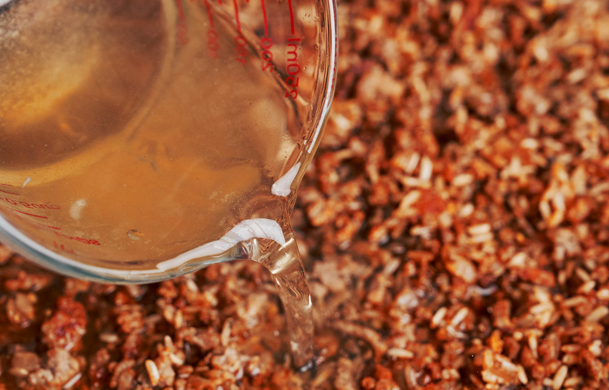 beef broth being poured into the skillet so the rice can simmer until tender