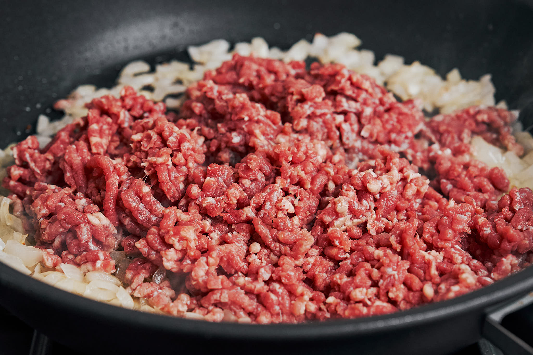 ground beef added to the skillet over the softened onion to start building a rich, hearty base