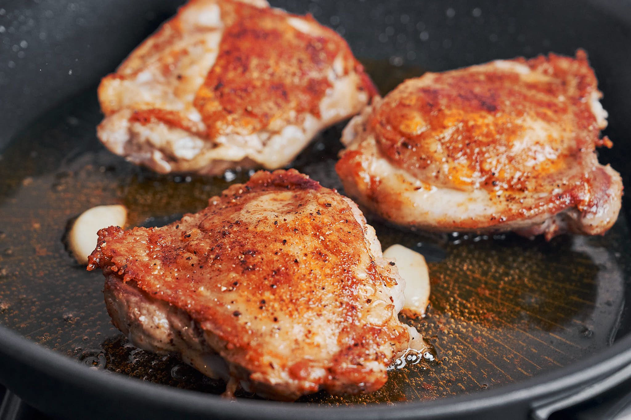 golden chicken thighs searing with garlic in olive oil