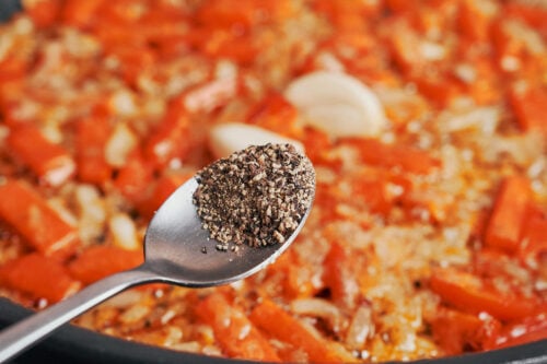 black pepper being added over the softened vegetables