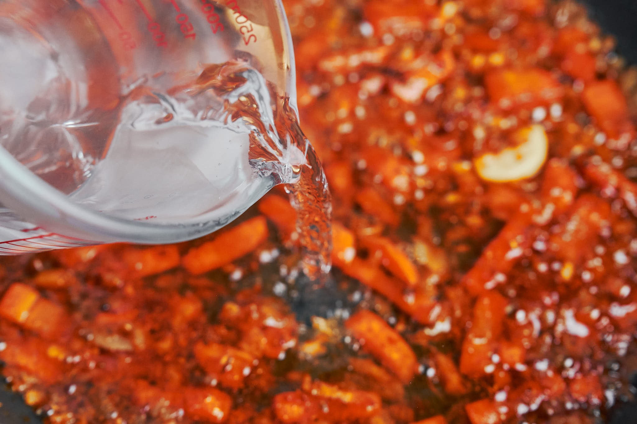 pouring boiling water into the skillet over the spiced vegetables