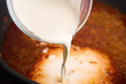 pouring heavy cream into the sauce to make it creamy