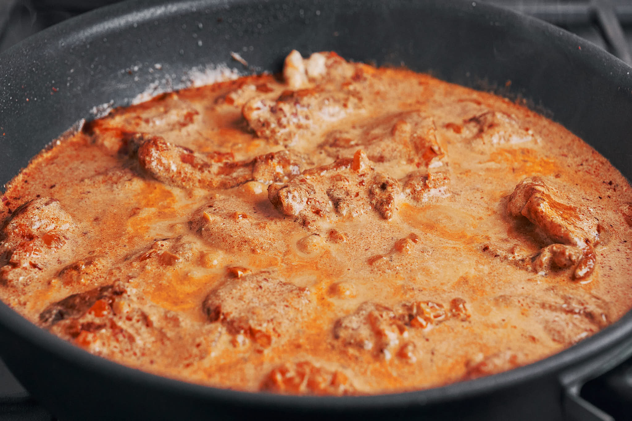 chicken simmering in creamy paprika sauce in skillet