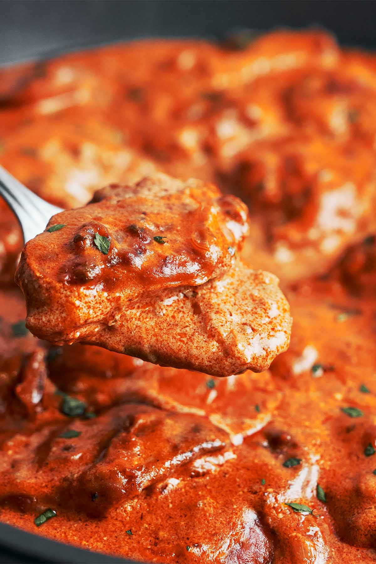 a spoon lifting tender chicken coated in creamy paprika sauce