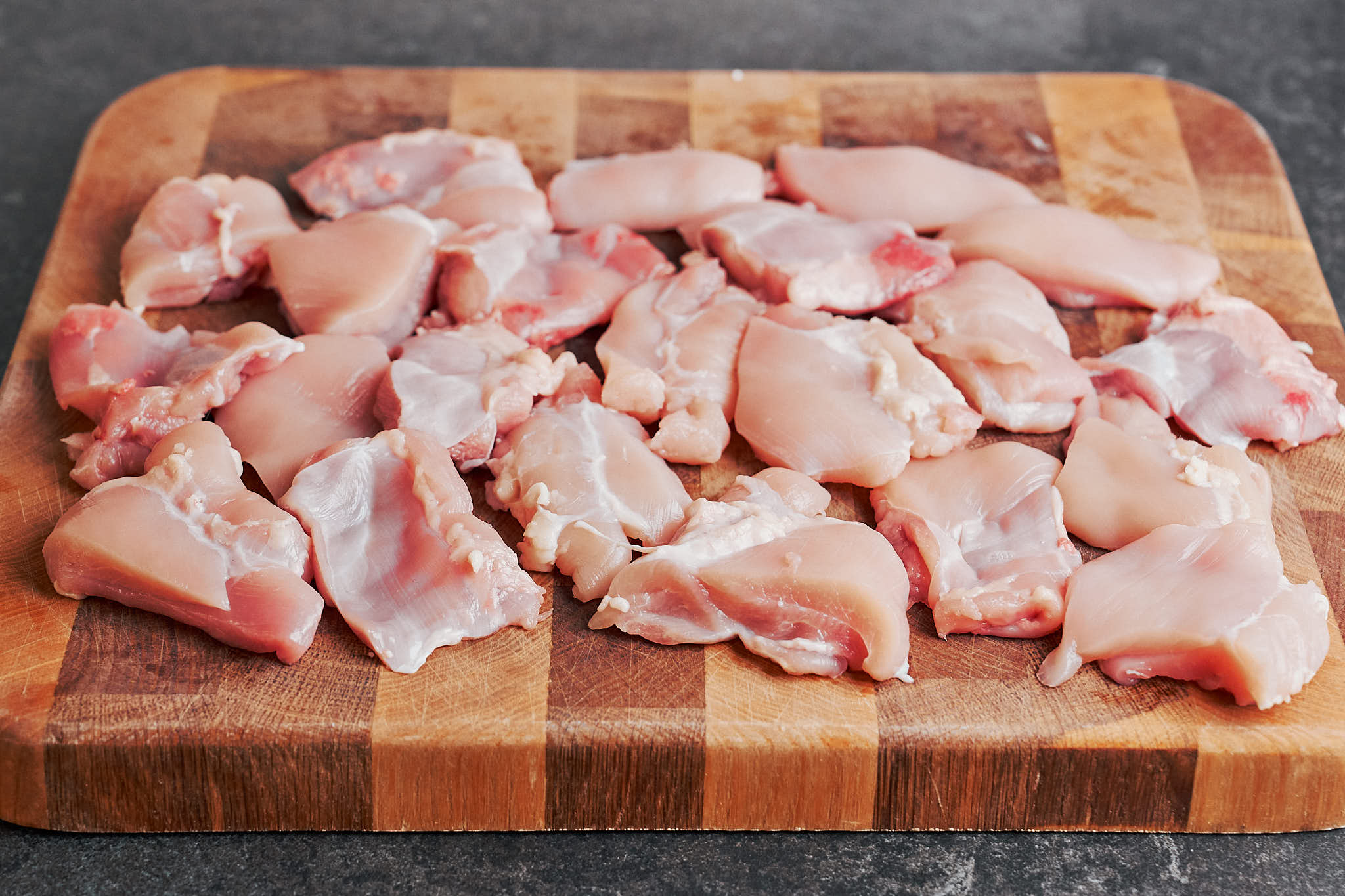raw boneless skinless chicken thighs cut into pieces on a wooden cutting board