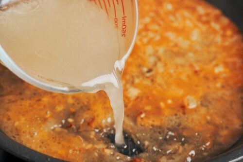 pouring chicken broth as the sauce begins to come together