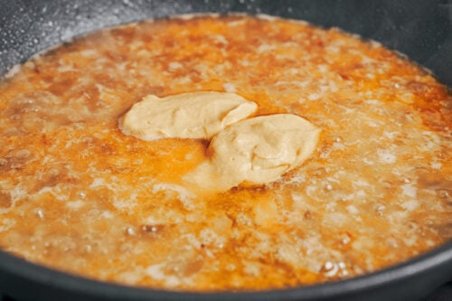 a spoon of Dijon mustard going into the sauce for that classic creamy flavor