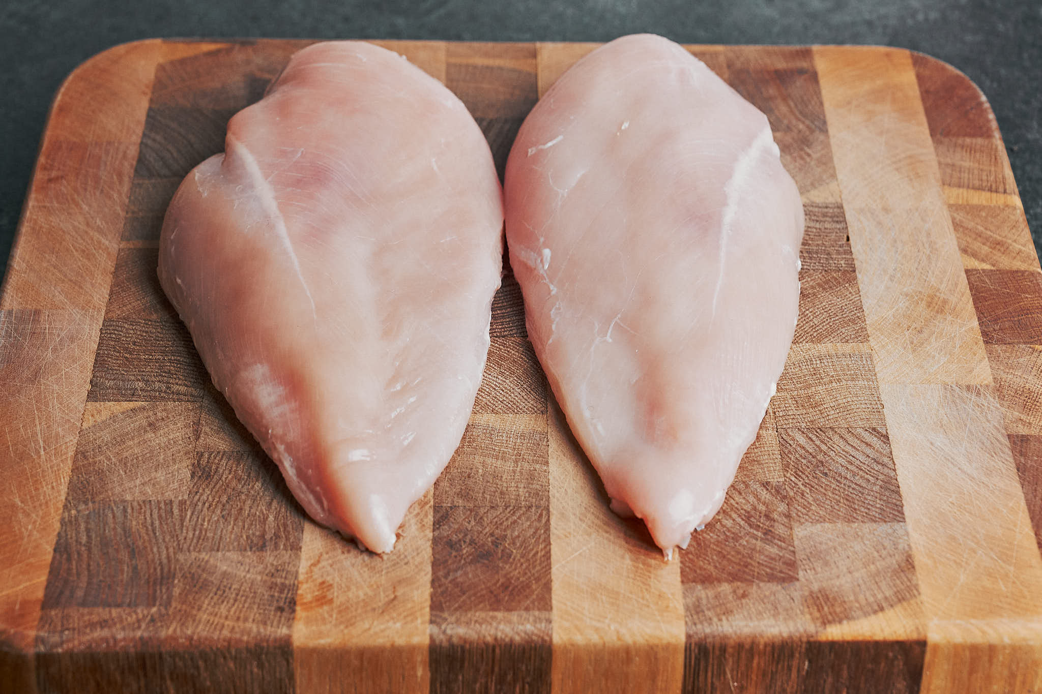 two raw chicken breasts on a cutting board before slicing them into thinner cutlets