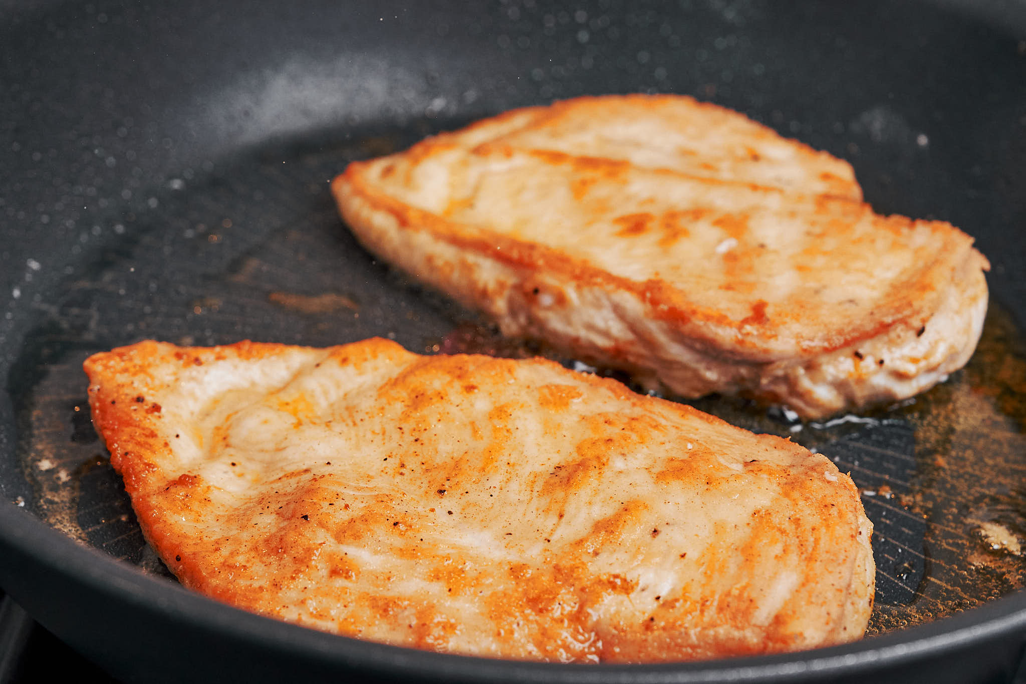 chicken cutlets cooking in a hot skillet to develop a golden crust