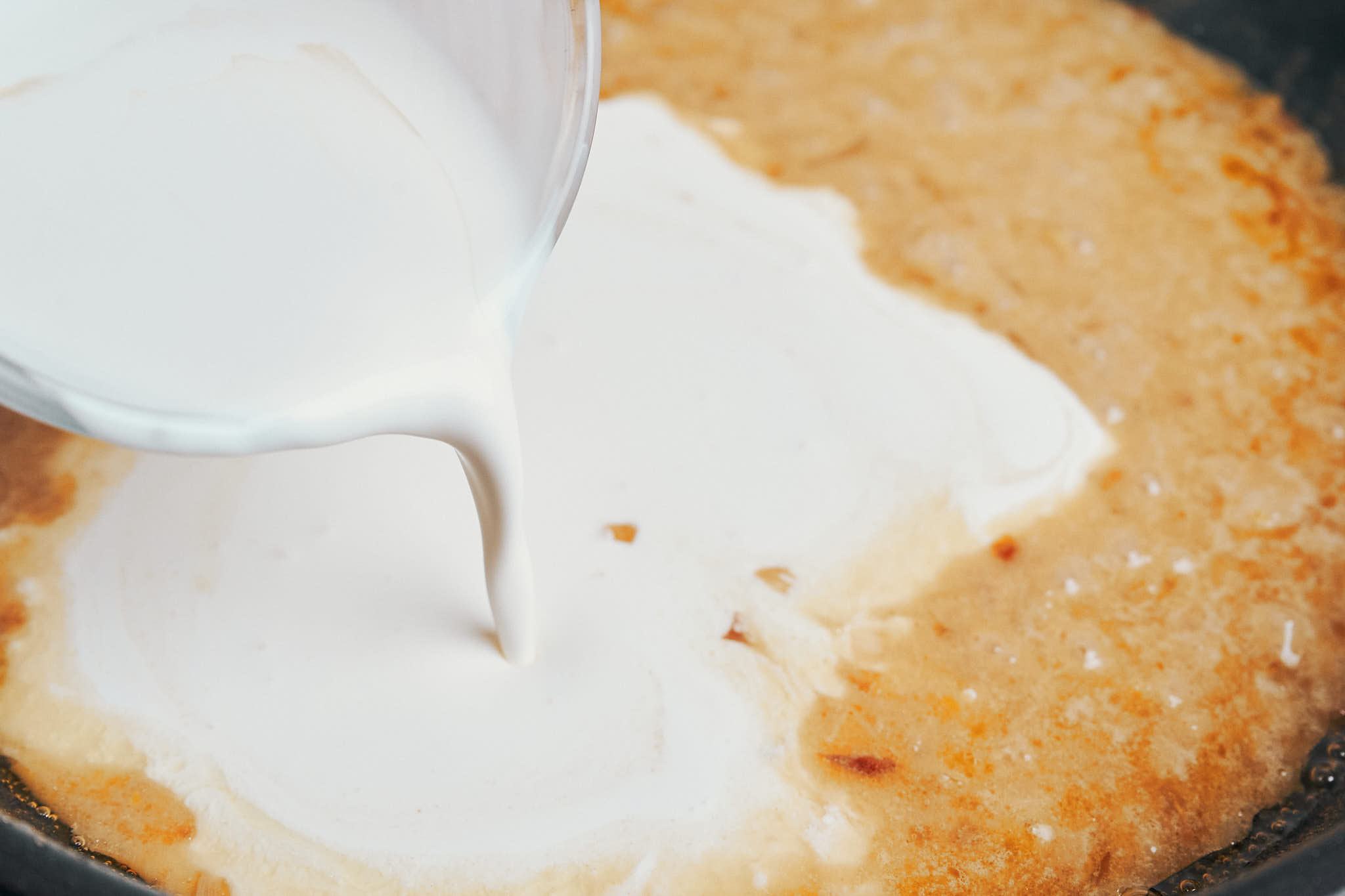 pouring heavy cream into the skillet to make the sauce rich and creamy
