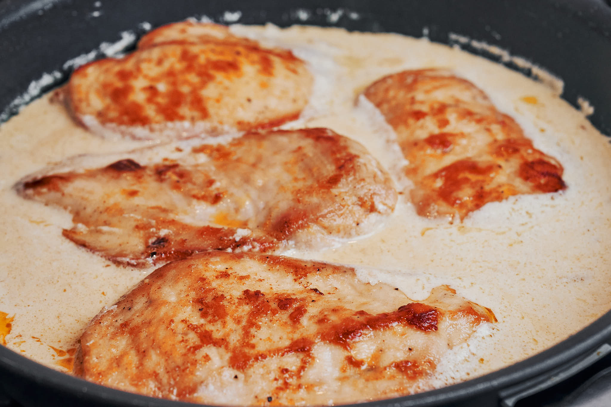 chicken simmering in a creamy lemon sauce in the skillet