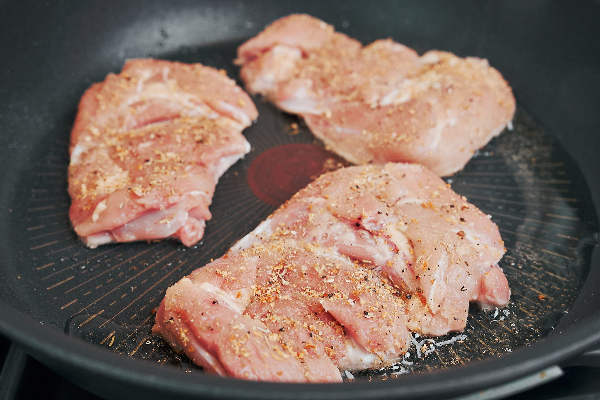 chicken thighs cooking in a skillet before turning golden