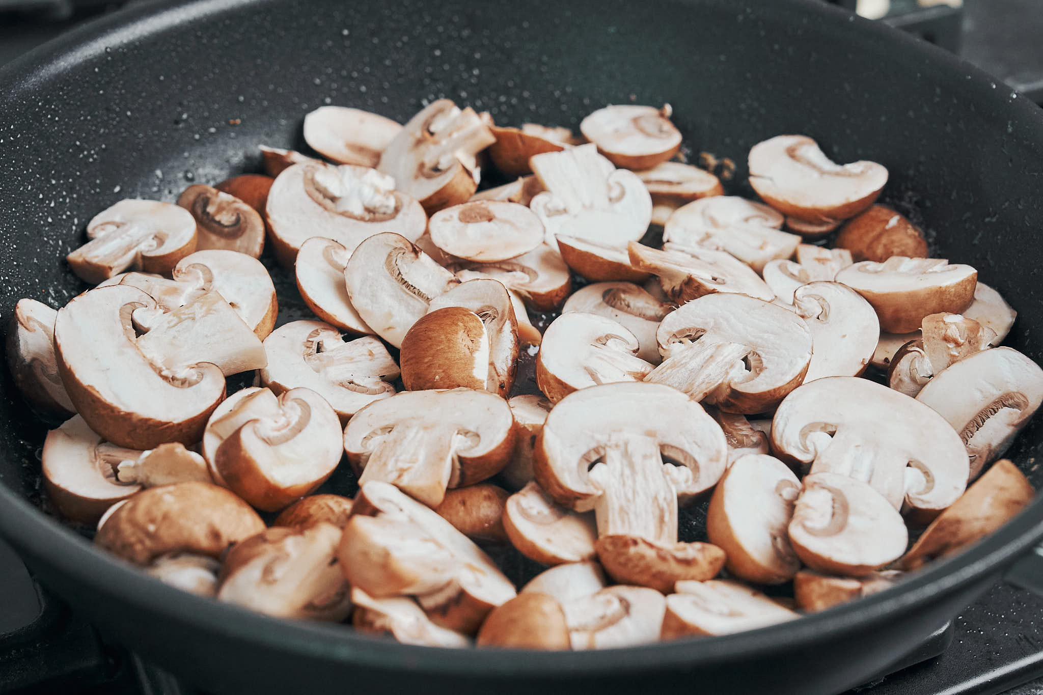 fresh sliced cremini mushrooms added to a skillet
