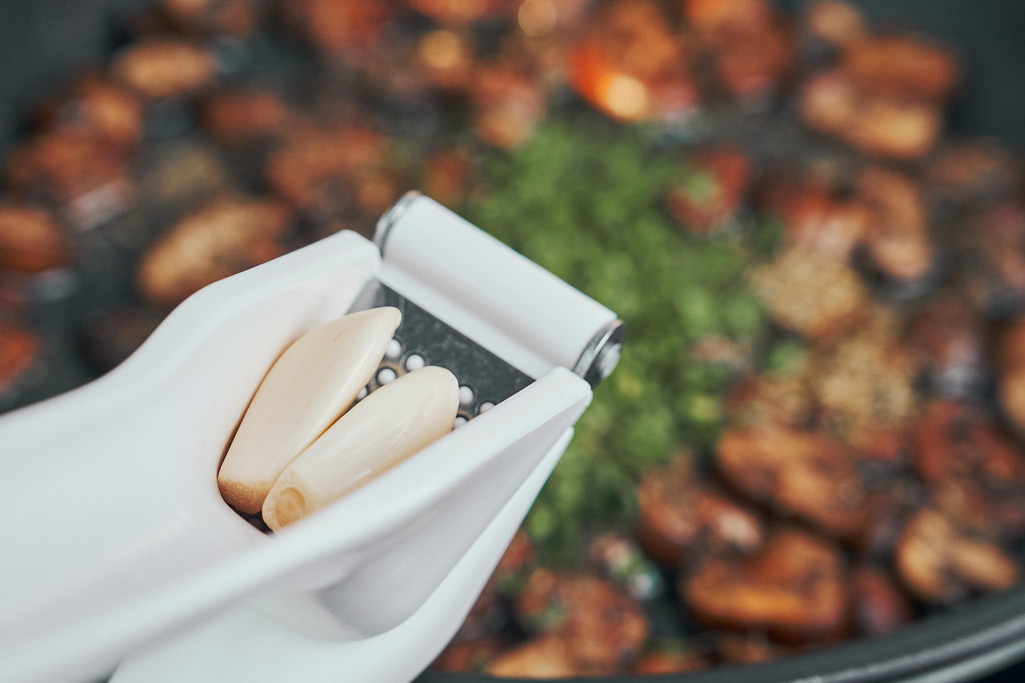 garlic being pressed into sautéed mushrooms