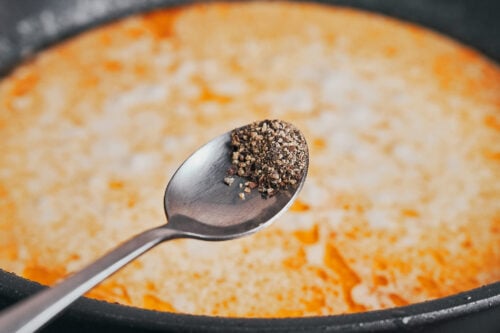 adding black pepper to the creamy sauce
