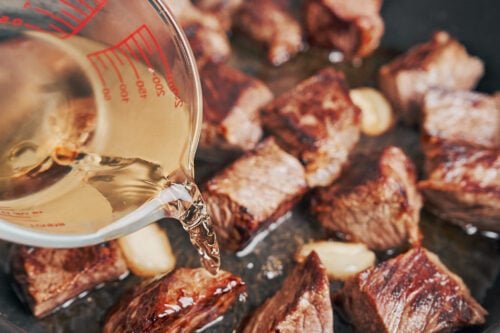 pouring wine into the pan after browning the beef