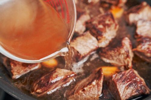 pouring beef stock over seared beef to build the stew