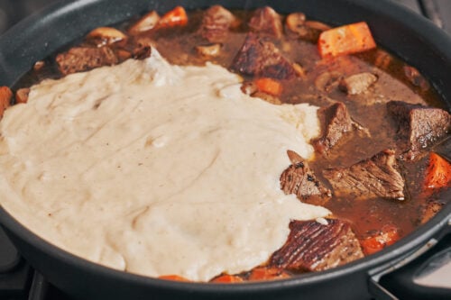 creamy sauce being poured over the beef stew