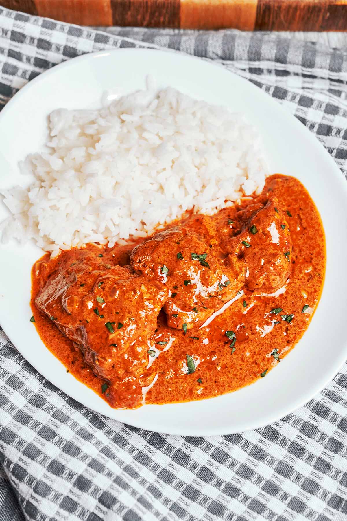 Creamy butter chicken served with white rice on a plate with rich tomato cream sauce and fresh parsley
