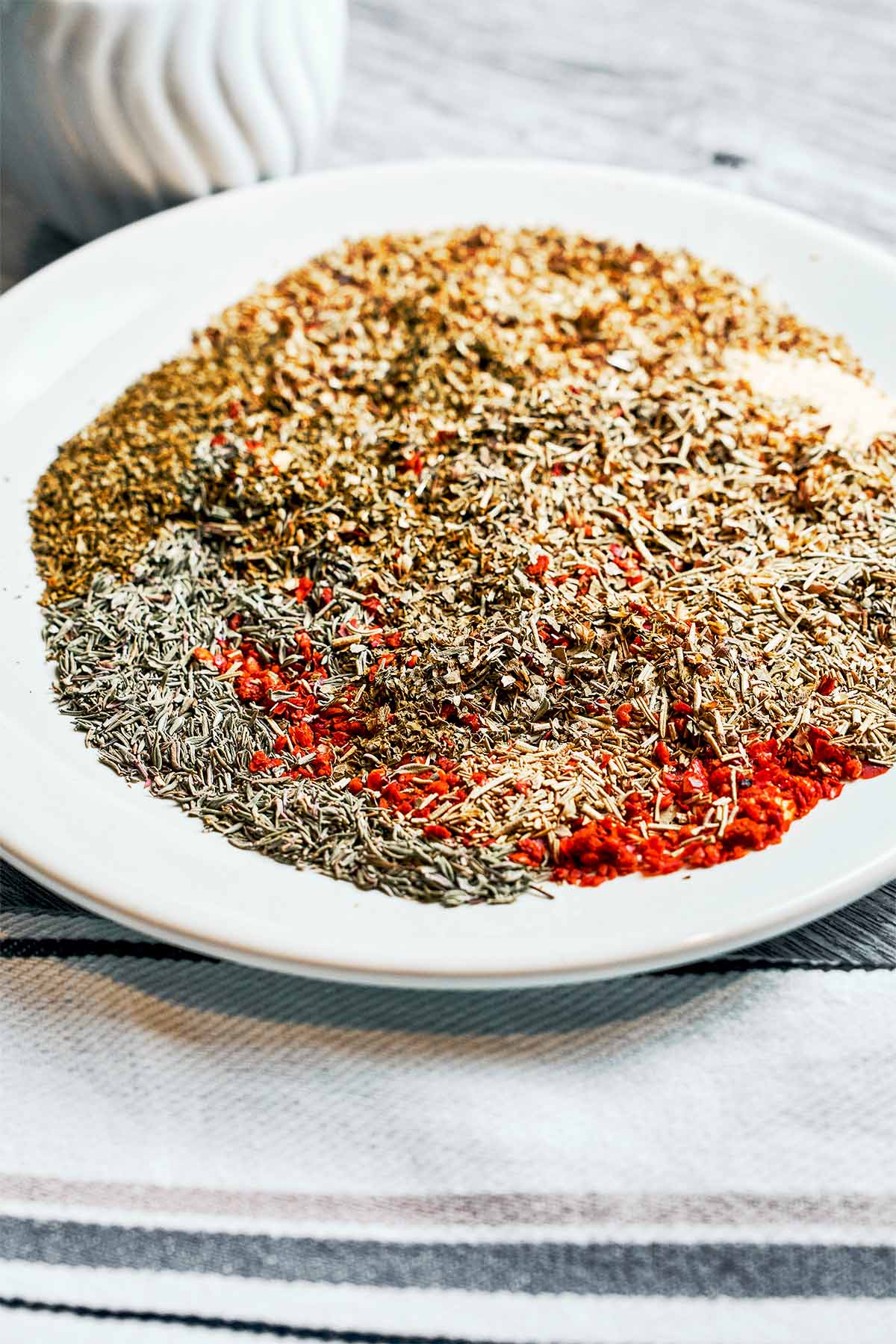 italian seasoning ingredients dried herbs and spices on white plate close up