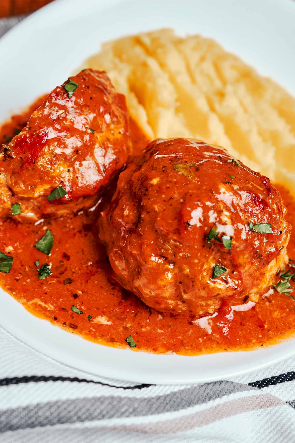 Juicy baked meatballs in rich tomato sauce served with creamy mashed potatoes