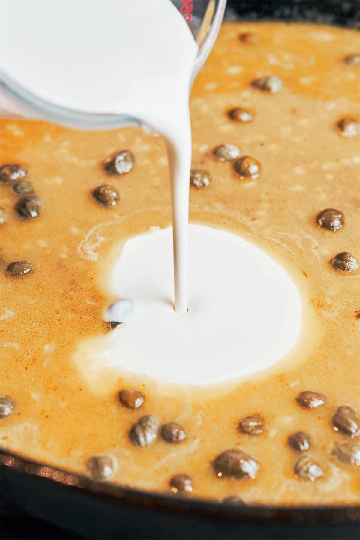 Heavy cream being poured into the lemon caper sauce to make it smooth, creamy, and silky.