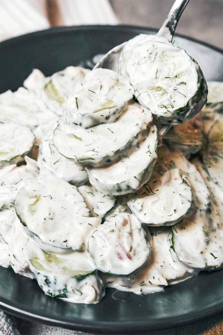 Creamy cucumber salad with crisp cucumber slices, fresh dill, red onion, and sour cream dressing on a spoon.