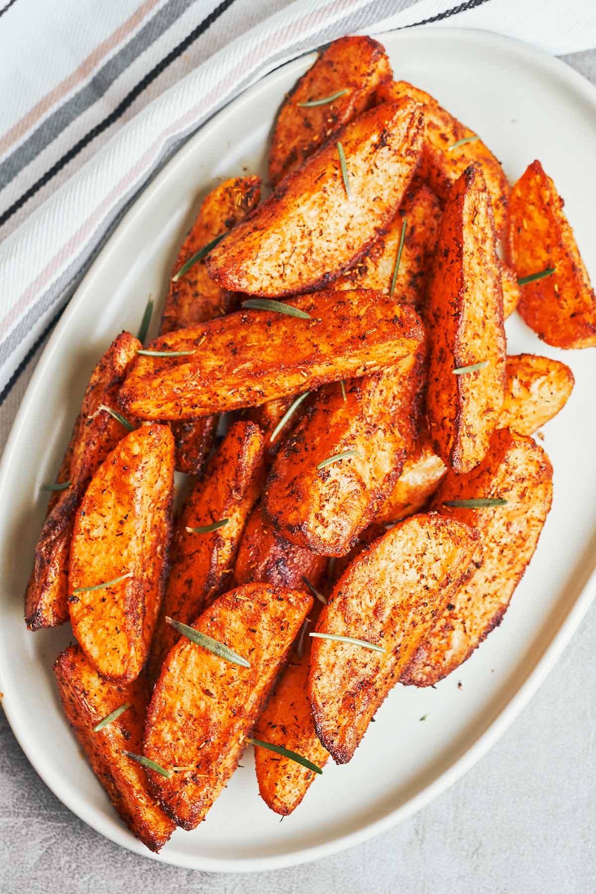 Oven roasted potato wedges with smoky garlic seasoning and rosemary served on an oval platter