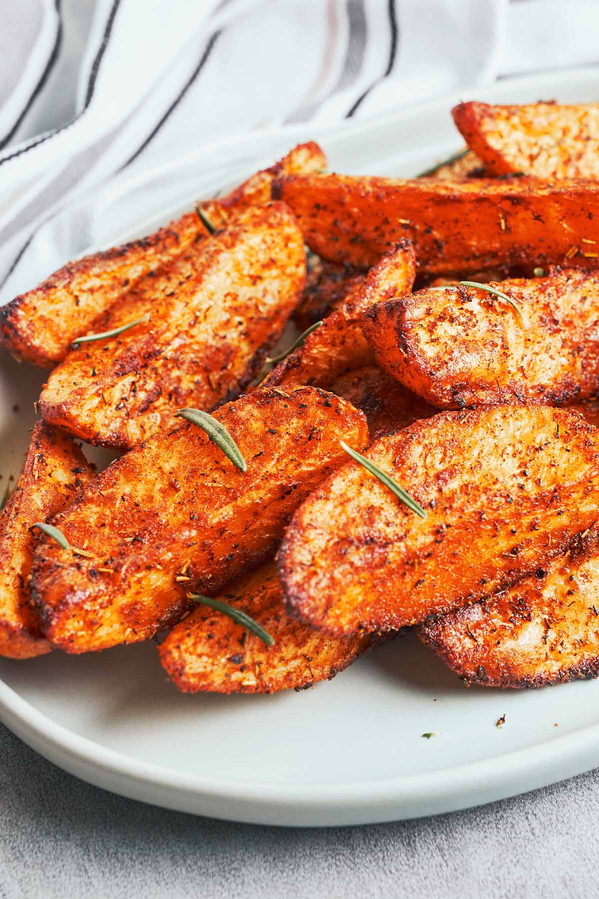 Deeply golden potato wedges with crisp seasoned edges and fresh rosemary arranged on a white serving plate