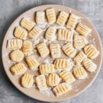 Fresh homemade gnocchi shaped with fork ridges and dusted with flour on a plate.