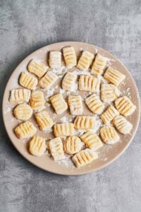 Fresh homemade gnocchi shaped with fork ridges and dusted with flour on a plate.