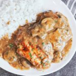 Smothered chicken with mushroom gravy served with fluffy white rice, tender mushrooms, and fresh parsley on a white plate.
