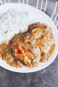 Smothered chicken with mushroom gravy served with fluffy white rice, tender mushrooms, and fresh parsley on a white plate.