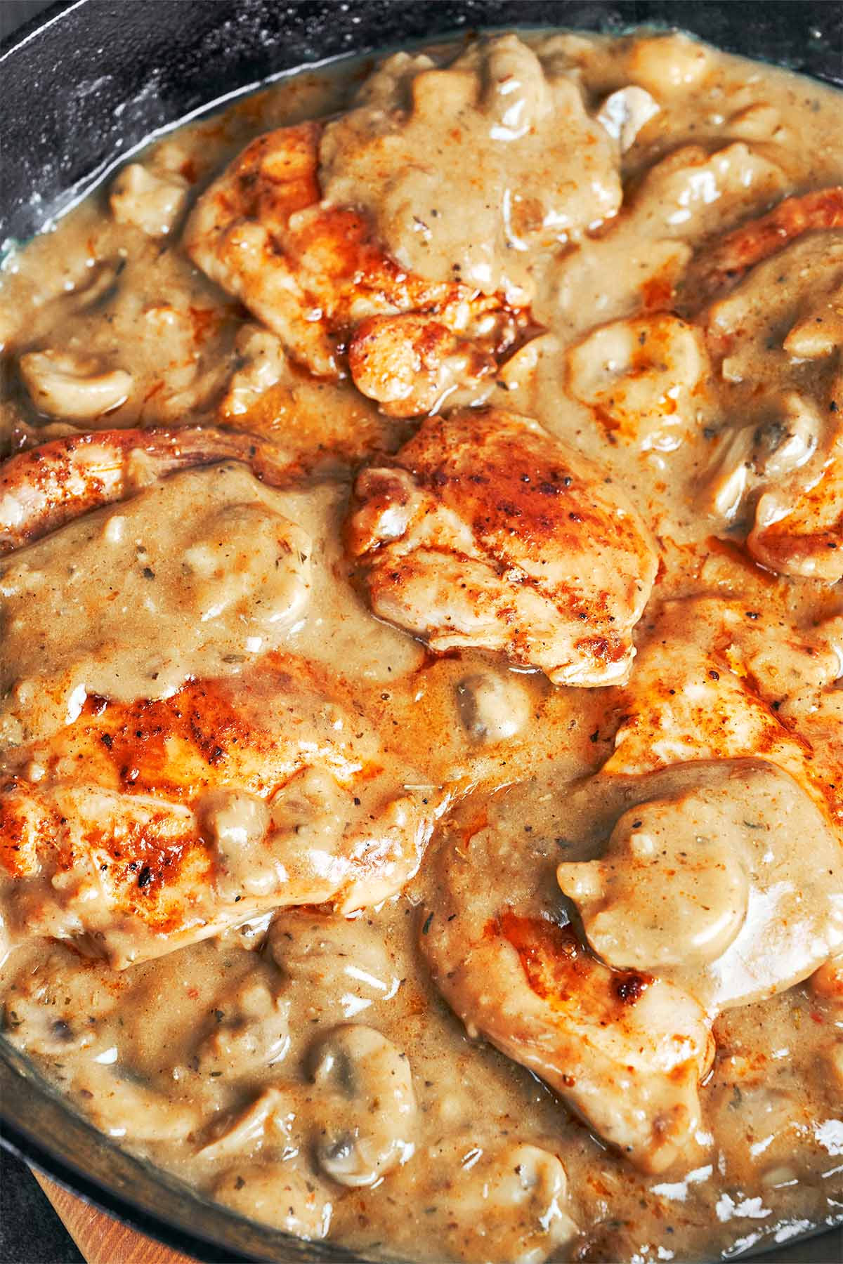Seared chicken thighs simmering in thick mushroom gravy with tender sliced mushrooms in a cast iron skillet.