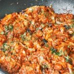 Braised cabbage with pork, smoky bacon, and prunes finished with fresh parsley in a large wok.