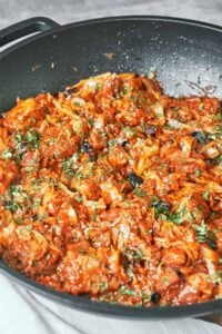 Braised cabbage with pork, smoky bacon, and prunes finished with fresh parsley in a large wok.