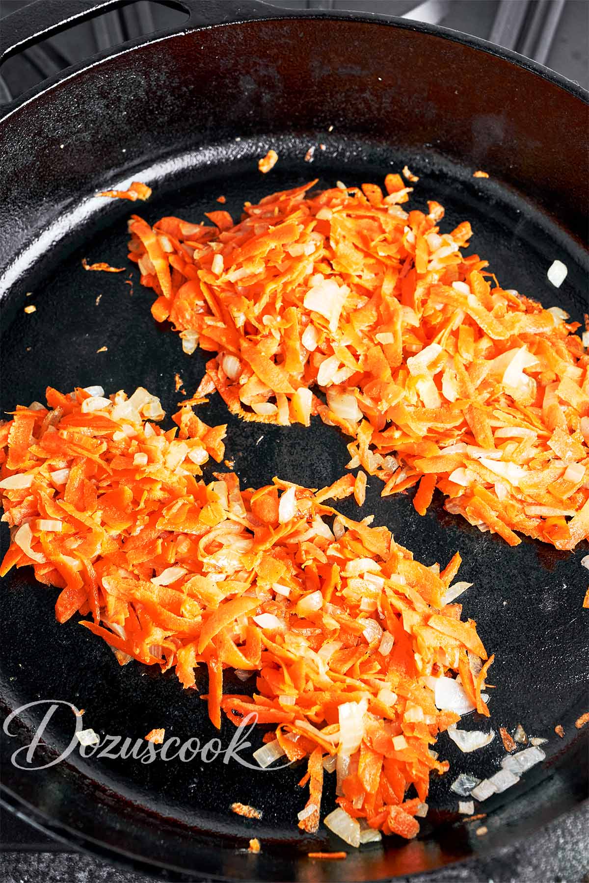 Sautéed onion and carrot divided in a skillet before adding to the meatballs