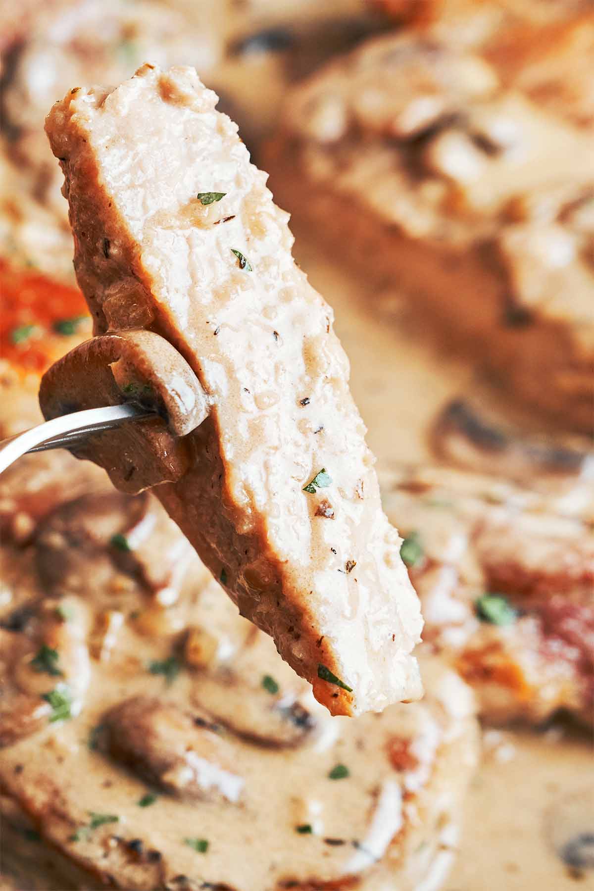 Juicy slice of pork chop coated in creamy Marsala sauce, with tender mushrooms and fresh parsley in the skillet below.