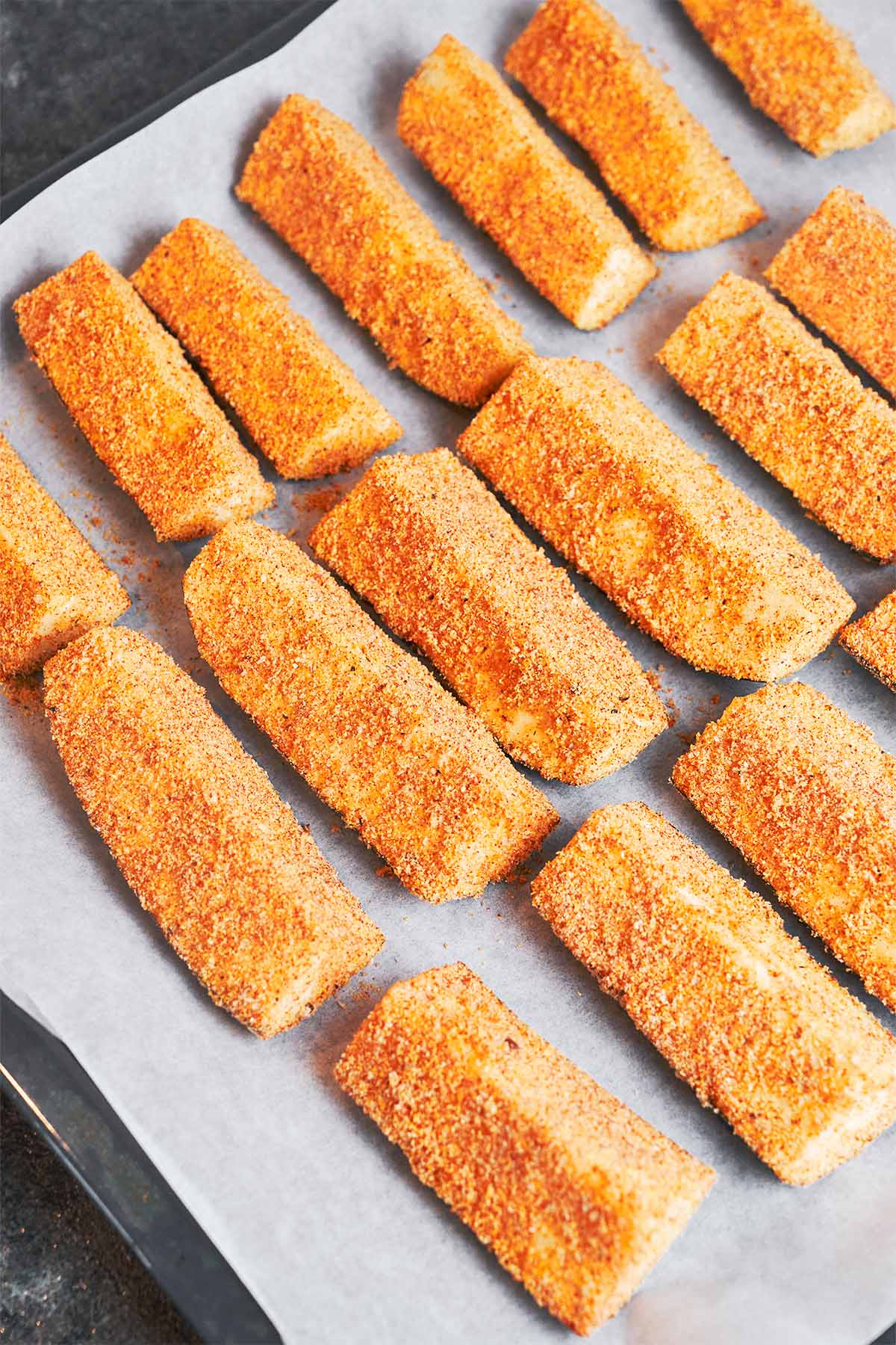 Breaded zucchini wedges arranged in a single layer on parchment, ready to bake until lightly golden and tender.