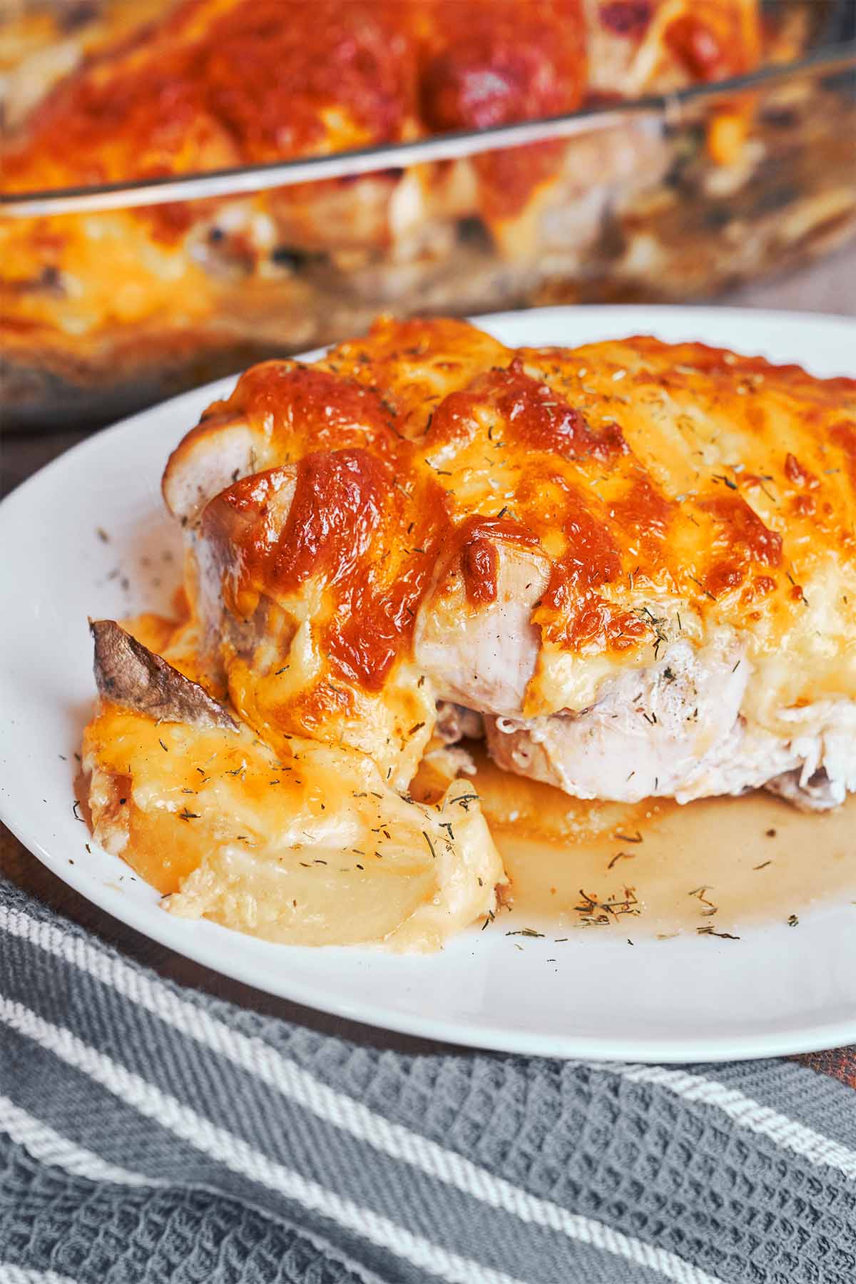 Easy baked chicken breast with golden melted cheese, tender potatoes, and mushrooms served on a plate.