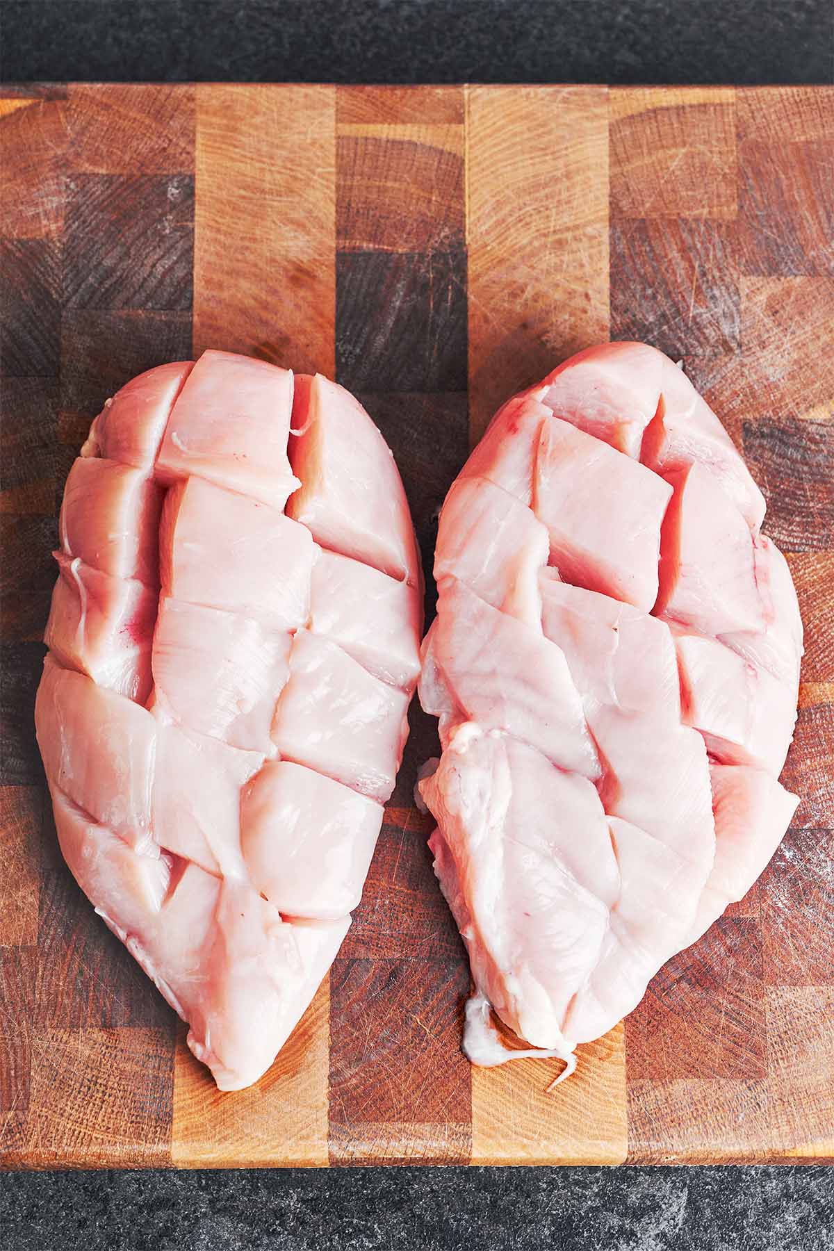 Two boneless chicken breasts with shallow crosshatch cuts, ready for the savory soy and sour cream sauce.