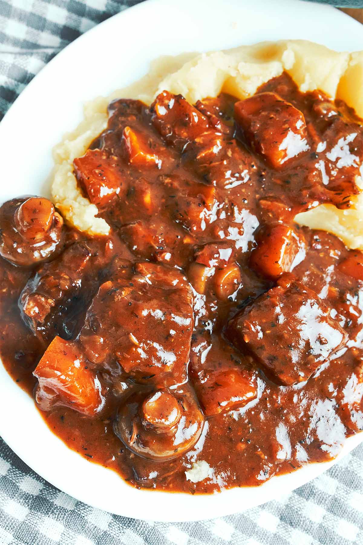 Cozy plate of pork bourguignon with tender pork, golden mushrooms, and carrots tucked into a rich red wine sauce over mashed potatoes.