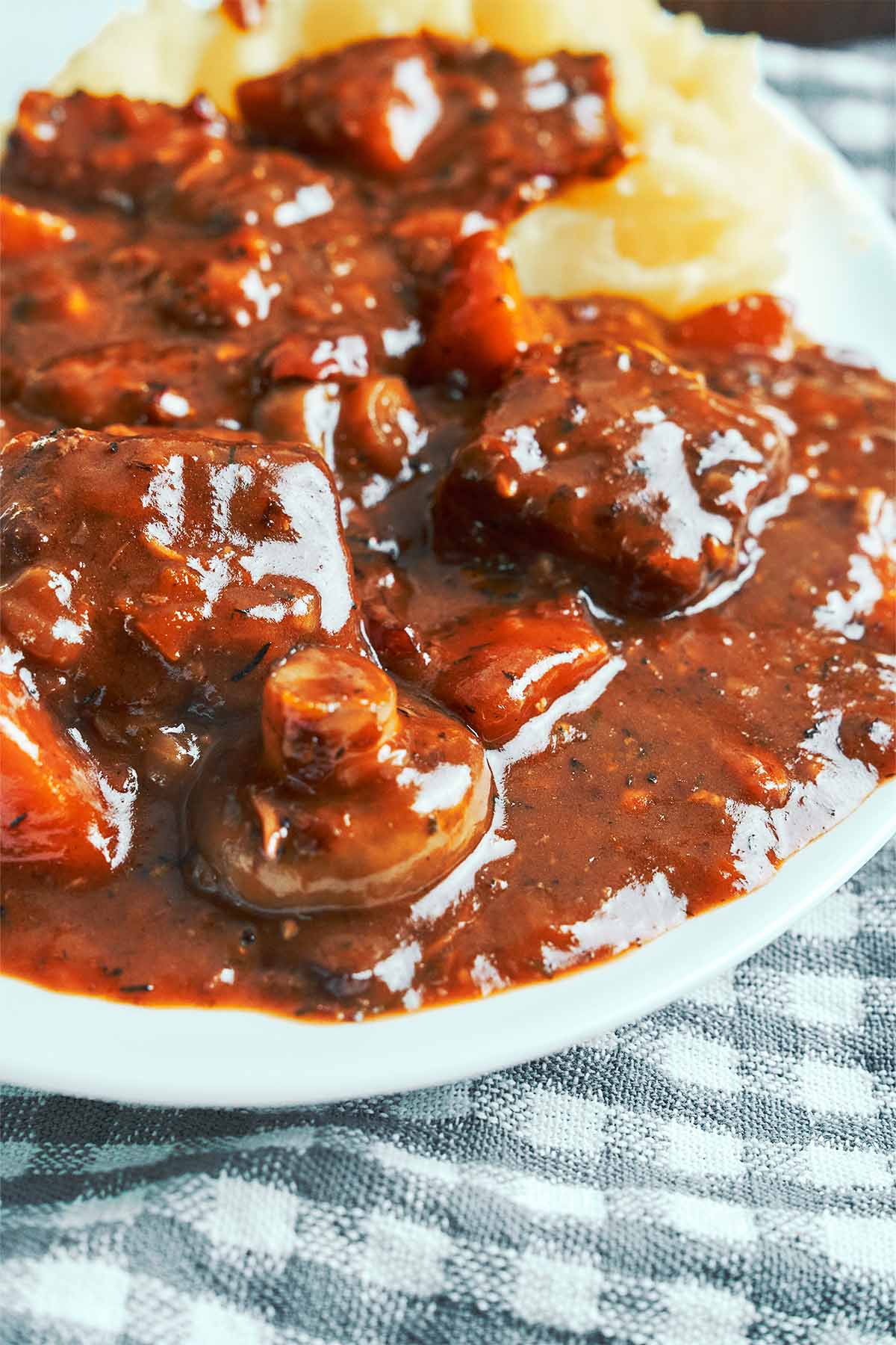Close-up of Pork Bourguignon with tender pork and golden mushrooms coated in a glossy red wine sauce, served with mashed potatoes.