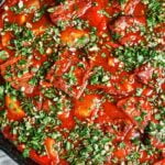 Beef stew with vegetables, potatoes, and carrots in a rich tomato sauce, finished with a generous scattering of fresh parsley and garlic.