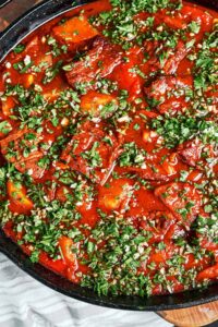 Beef stew with vegetables, potatoes, and carrots in a rich tomato sauce, finished with a generous scattering of fresh parsley and garlic.