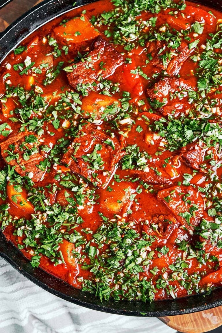 Beef stew with vegetables, potatoes, and carrots in a rich tomato sauce, finished with a generous scattering of fresh parsley and garlic.