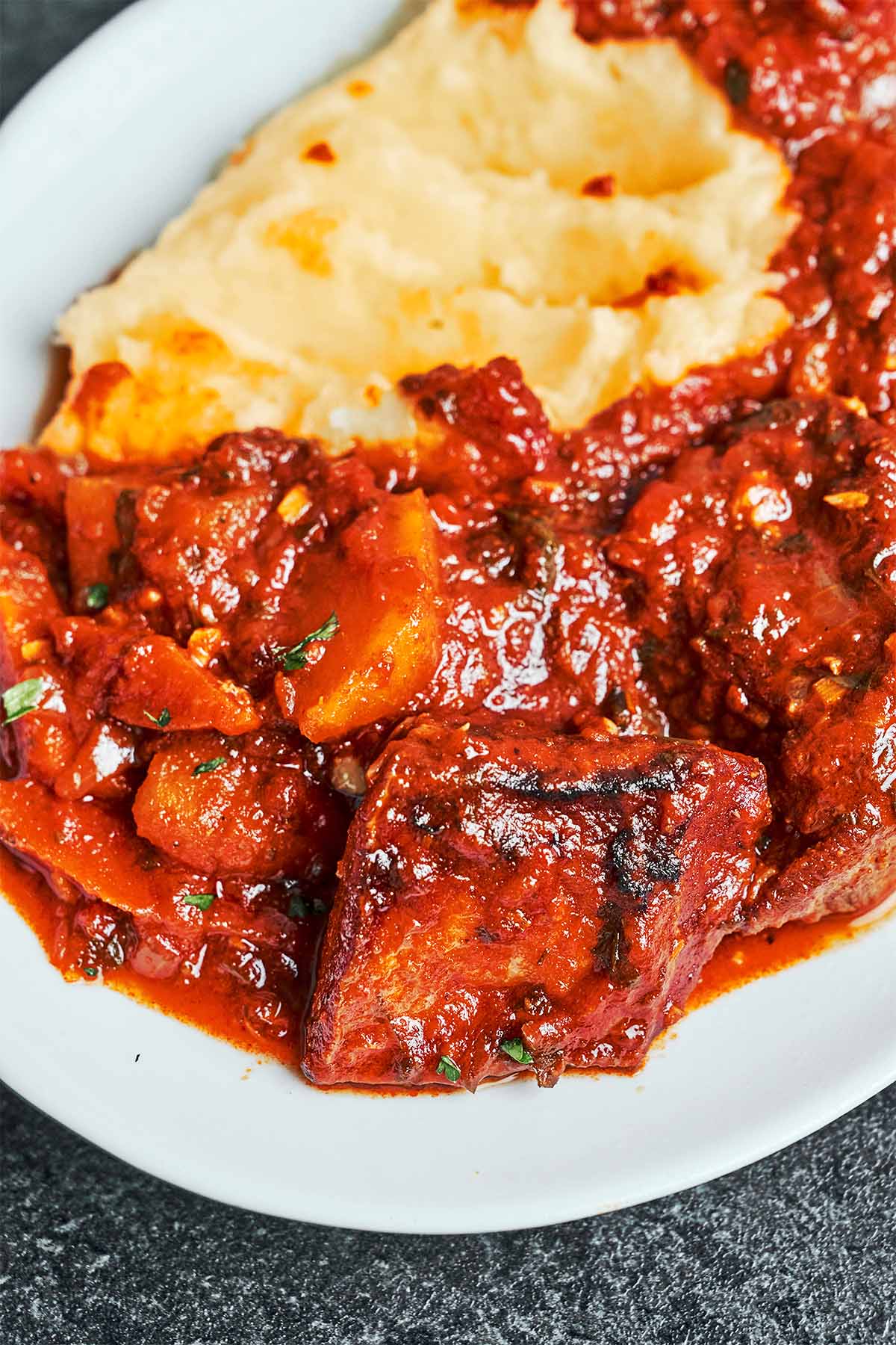 Beef stew with vegetables in a rich tomato sauce, served alongside creamy mashed potatoes with a sprinkle of parsley.